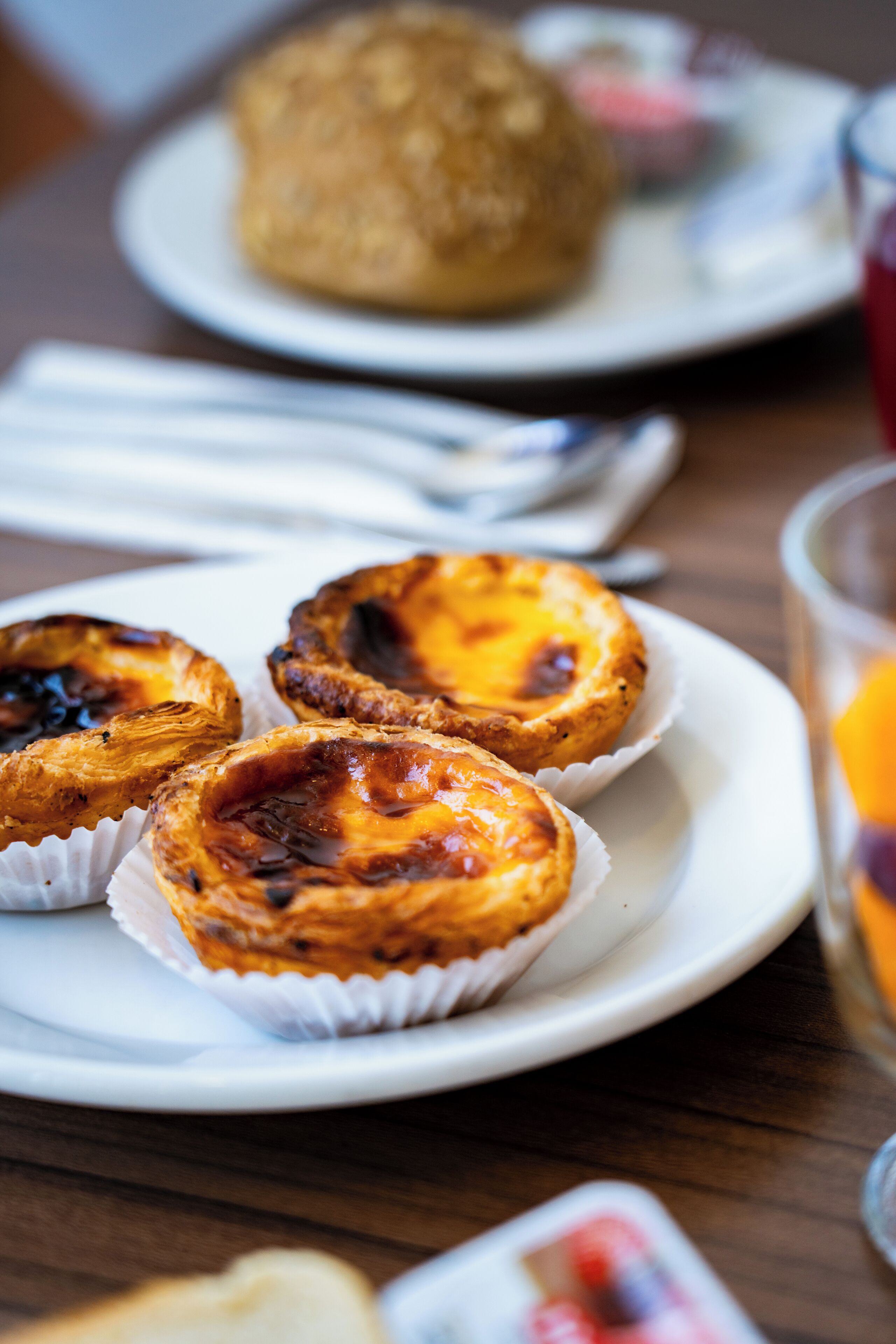 Une assiette contenant trois pasteis de nata (tartelettes aux œufs portugaises) et un muffin, posée sur une table en bois.