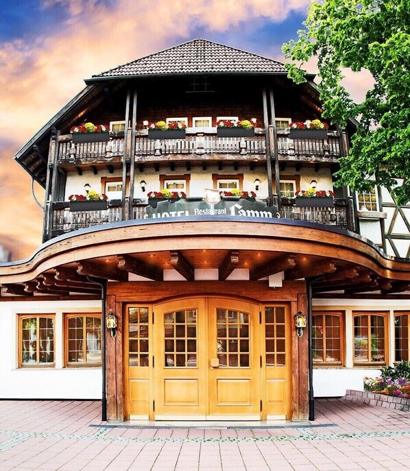 A traditional chalet-style hotel with a wooden facade, large windows, and a balcony with flower boxes.
