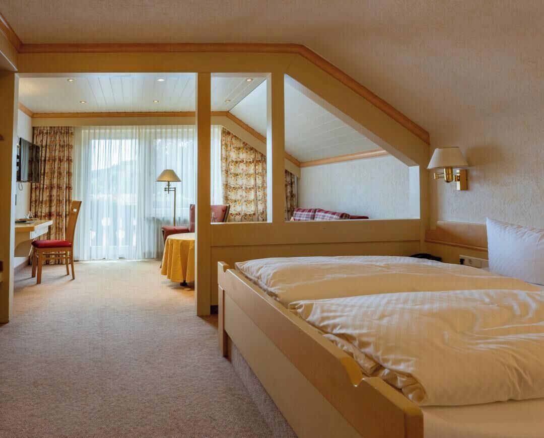 A hotel room with a large bed, a desk with a chair, a television, and a window with curtains.