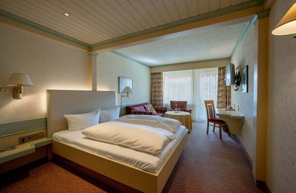 A hotel room with a large bed, bedside tables, a desk, and a chair. - Hotel Lamm (Baiersbronn)