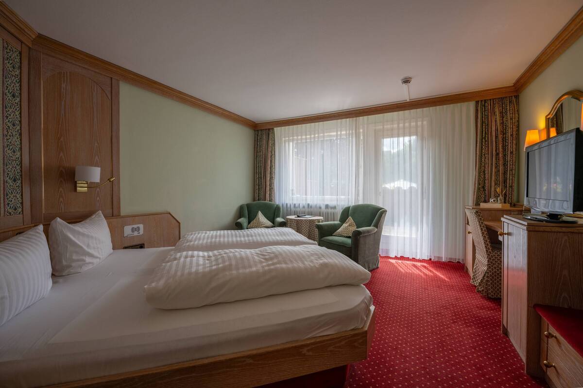 Una habitación de hotel con una cama grande, dos sillones, una mesita, un televisor y un escritorio con una computadora.