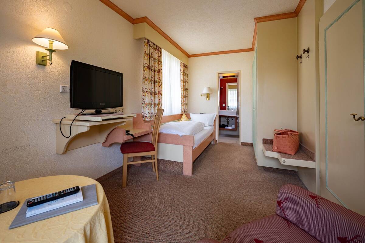 Habitación de hotel con cama, escritorio con computadora, televisor, silla, pequeña mesa con control remoto y sofá rojo.