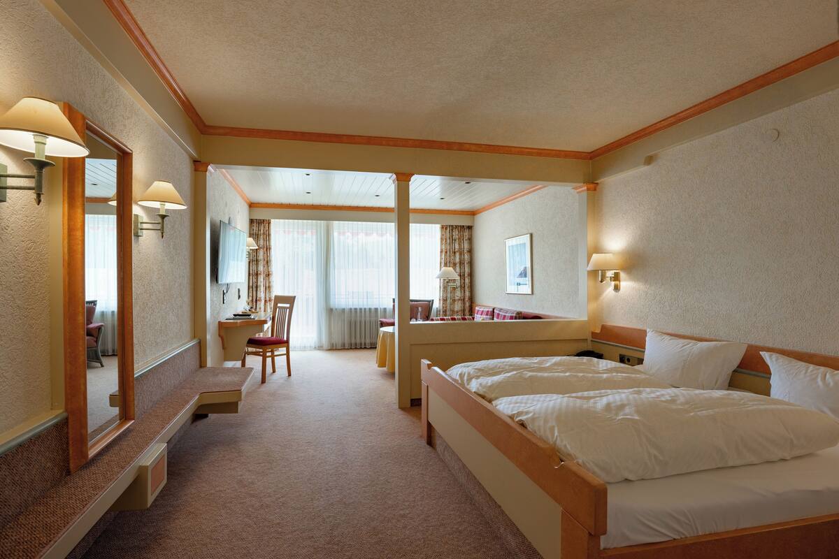 Habitación de hotel con una cama grande, un escritorio con silla, un espejo y vista al pasillo.