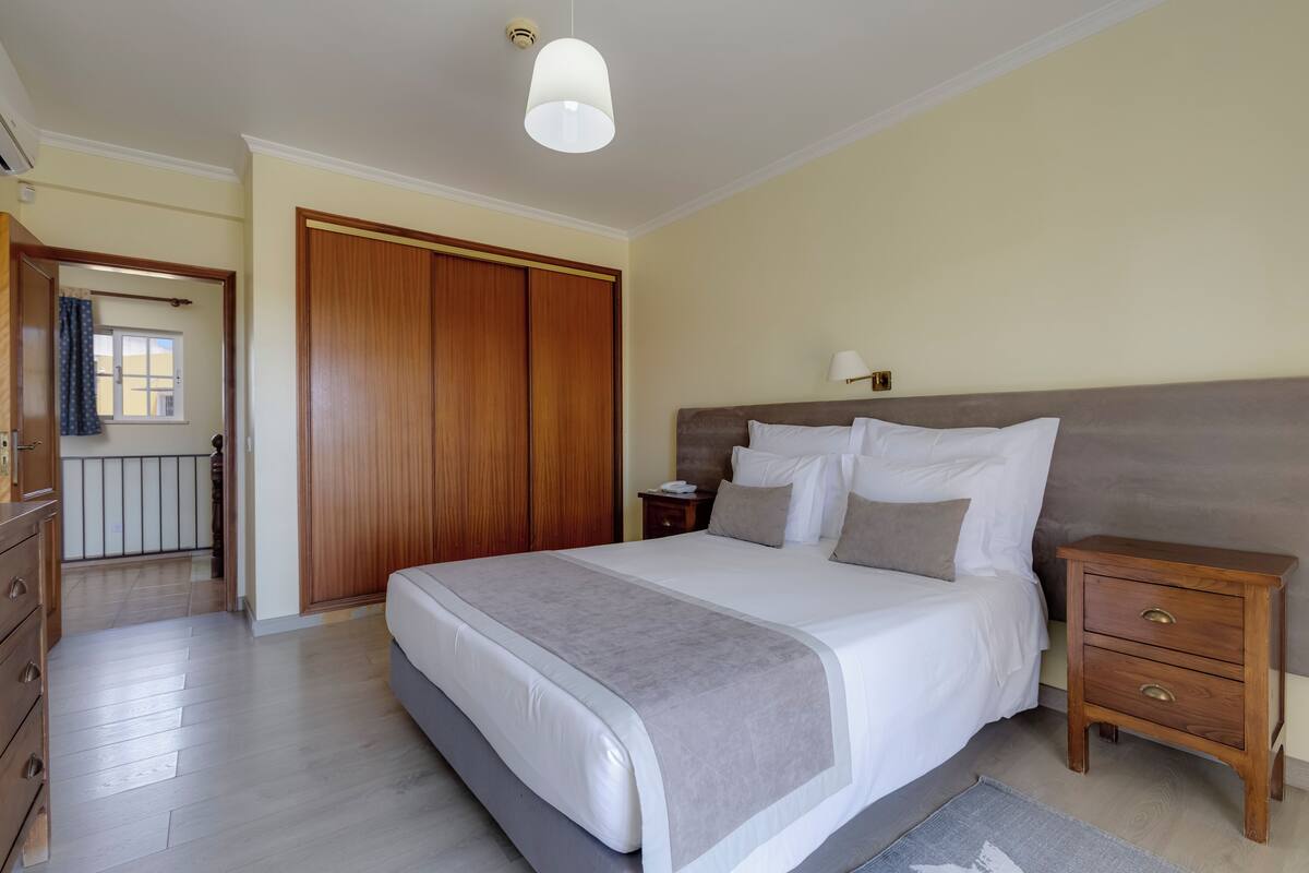 A bedroom with a large bed, wooden wardrobe, bedside tables, and a ceiling light.