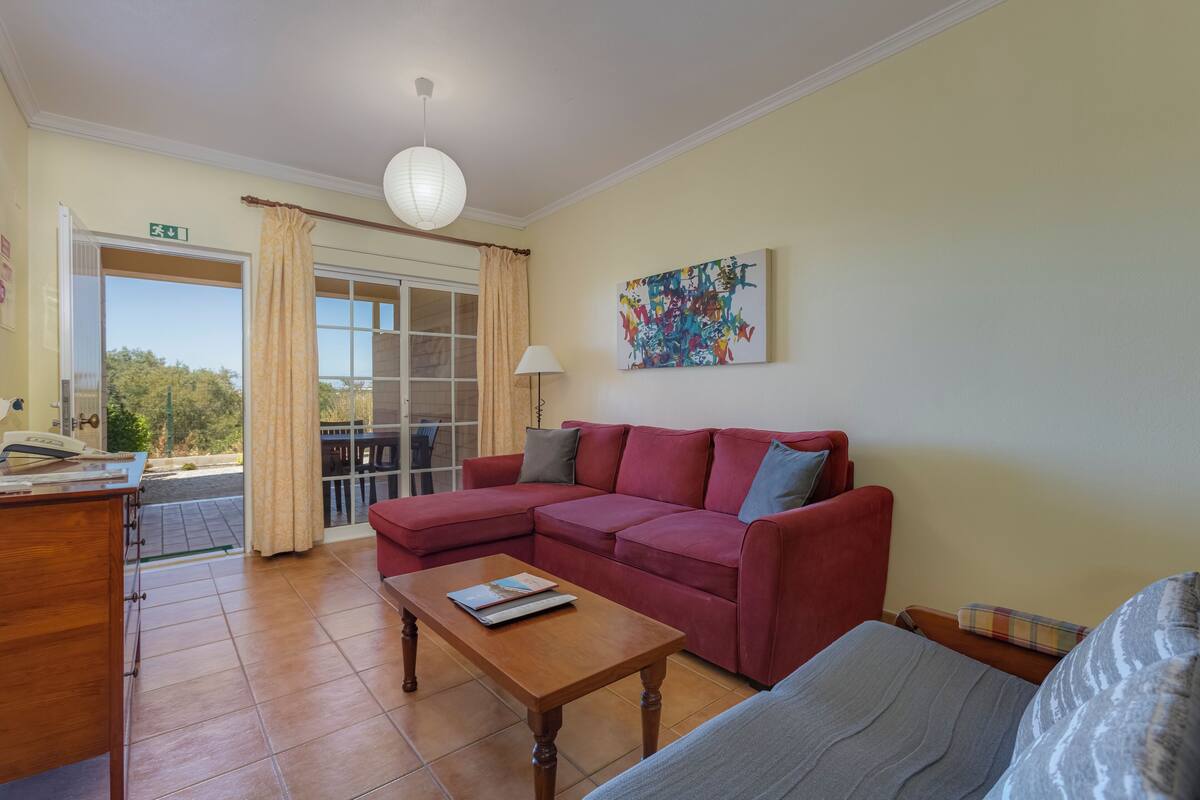 A living room with a red sectional sofa, a wooden coffee table, a lamp, and a colorful abstract painting.