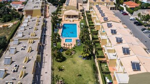 A residential area with a swimming pool surrounded by solar panels, a tennis court, and a street with parked cars. - Villas Barrocal (Silves)