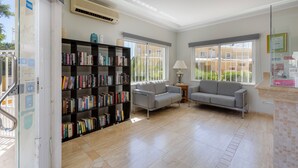 A spacious room with a large bookshelf, two grey sofas, and a window with a view of buildings. - Villas Barrocal (Silves)