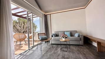 A modern living room with a grey sofa, wicker chairs, a small round table, and a large window with a view of cacti.
