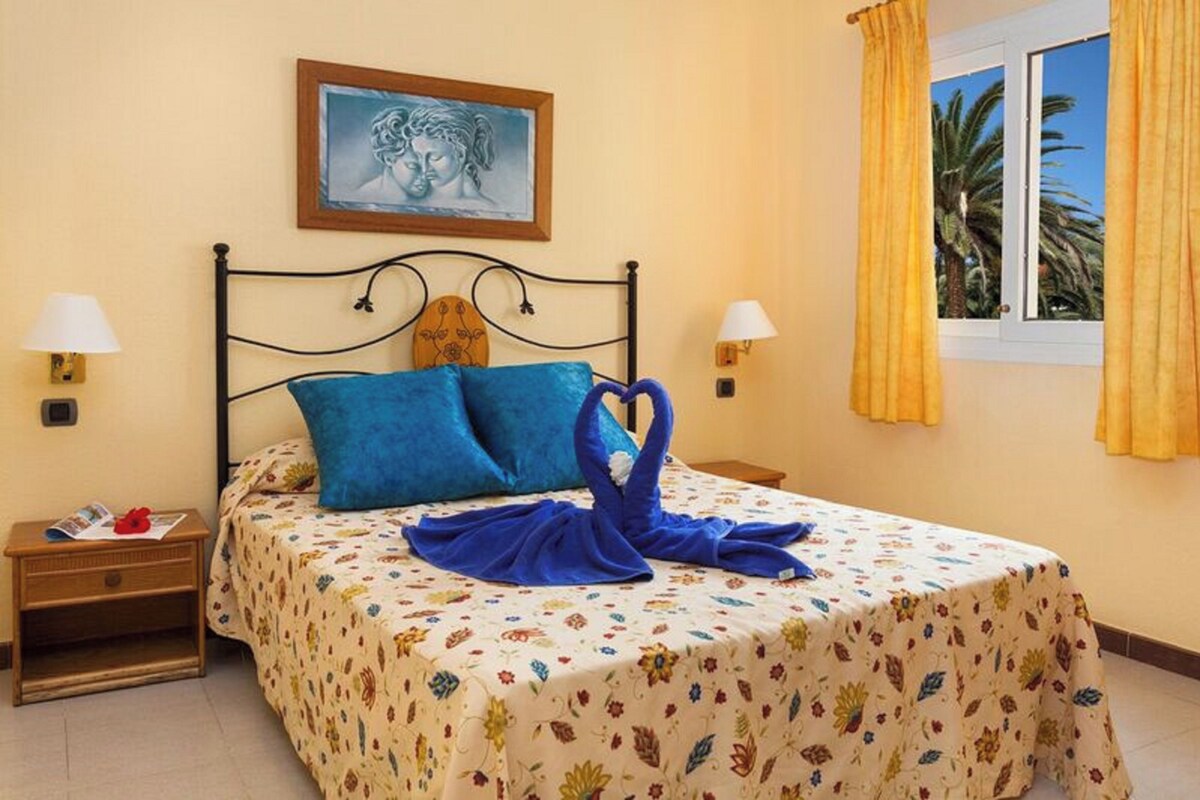 Une chambre à coucher avec un lit, deux tables de chevet, une commode, une fenêtre avec des rideaux et un tableau au mur.