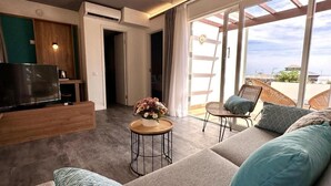 Una sala de estar moderna con un sofá, un televisor, una pequeña mesa redonda con un arreglo floral y un balcón con sillas de mimbre.