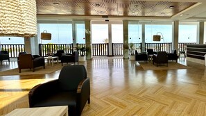 Un vaste espace intérieur doté de plusieurs types d’aménagements pour s’asseoir, d’un plafond au design ajouré et de grandes fenêtres offrant une vue dégagée.
