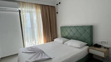 Quarto de hotel com uma cama, mesa de cabeceira, abajur e janela com cortinas.