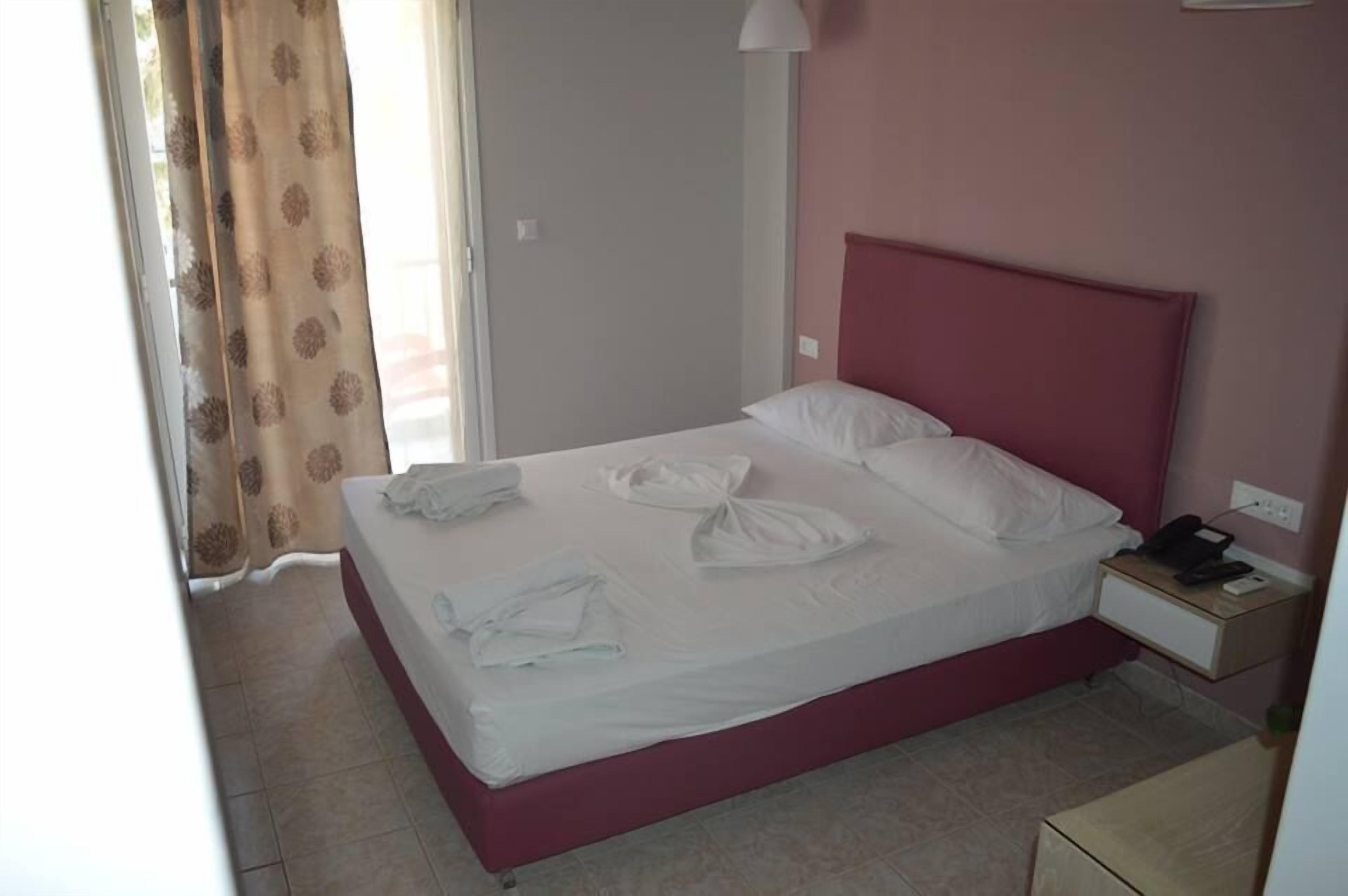 A neatly made bed with white linens and towels, a bedside table with a phone, and a nightstand with a lamp.