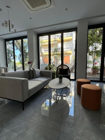 A modern living room with a sofa, a coffee table, and two ottomans. Large windows provide a view of the outside.