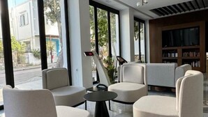 Un espace de détente moderne avec des canapés et une table basse, de grandes fenêtres donnant sur la rue et une bibliothèque remplie de livres.