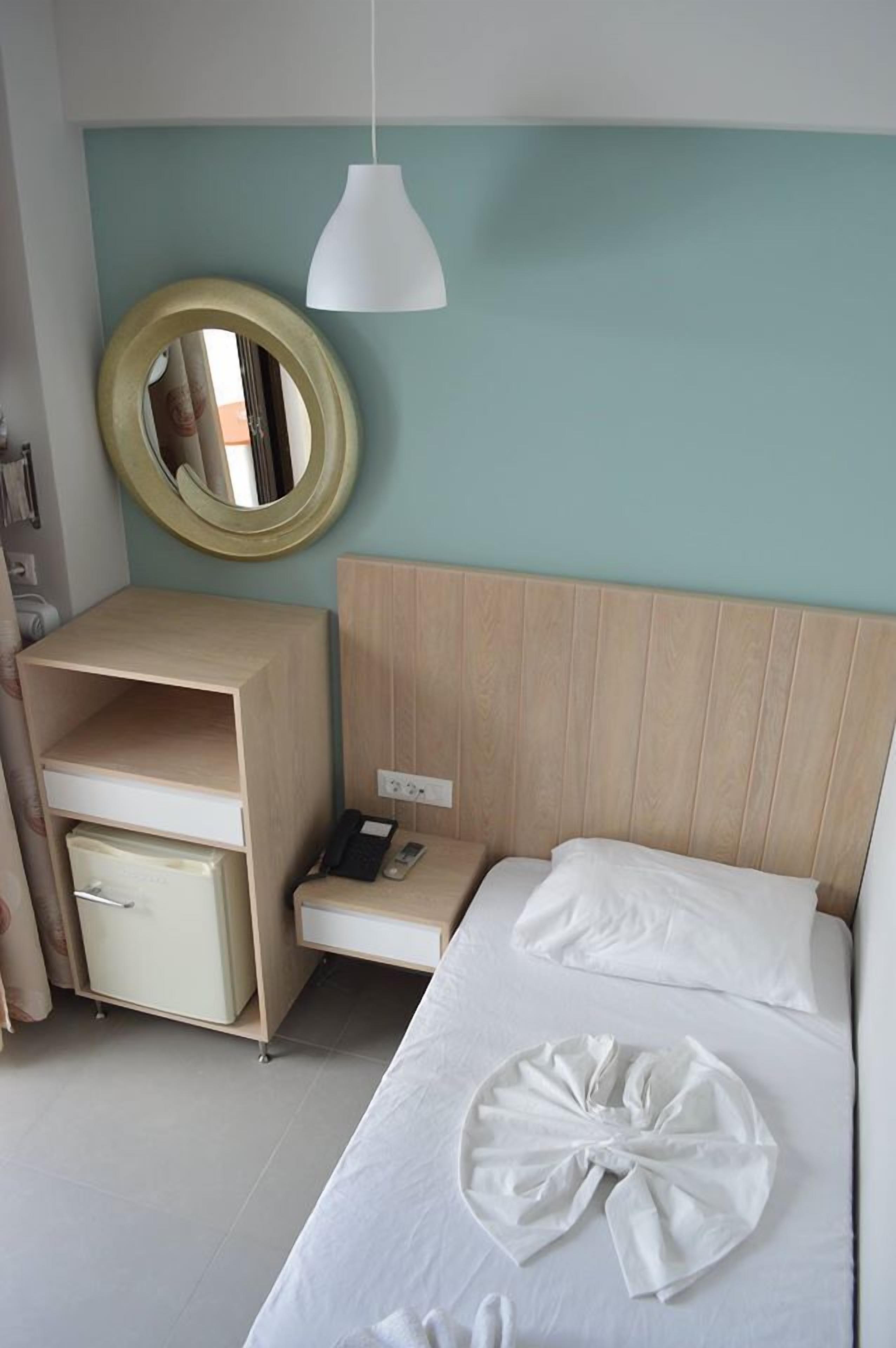A hotel room with a bed, a bedside table, a lamp, a mirror, and a wardrobe.