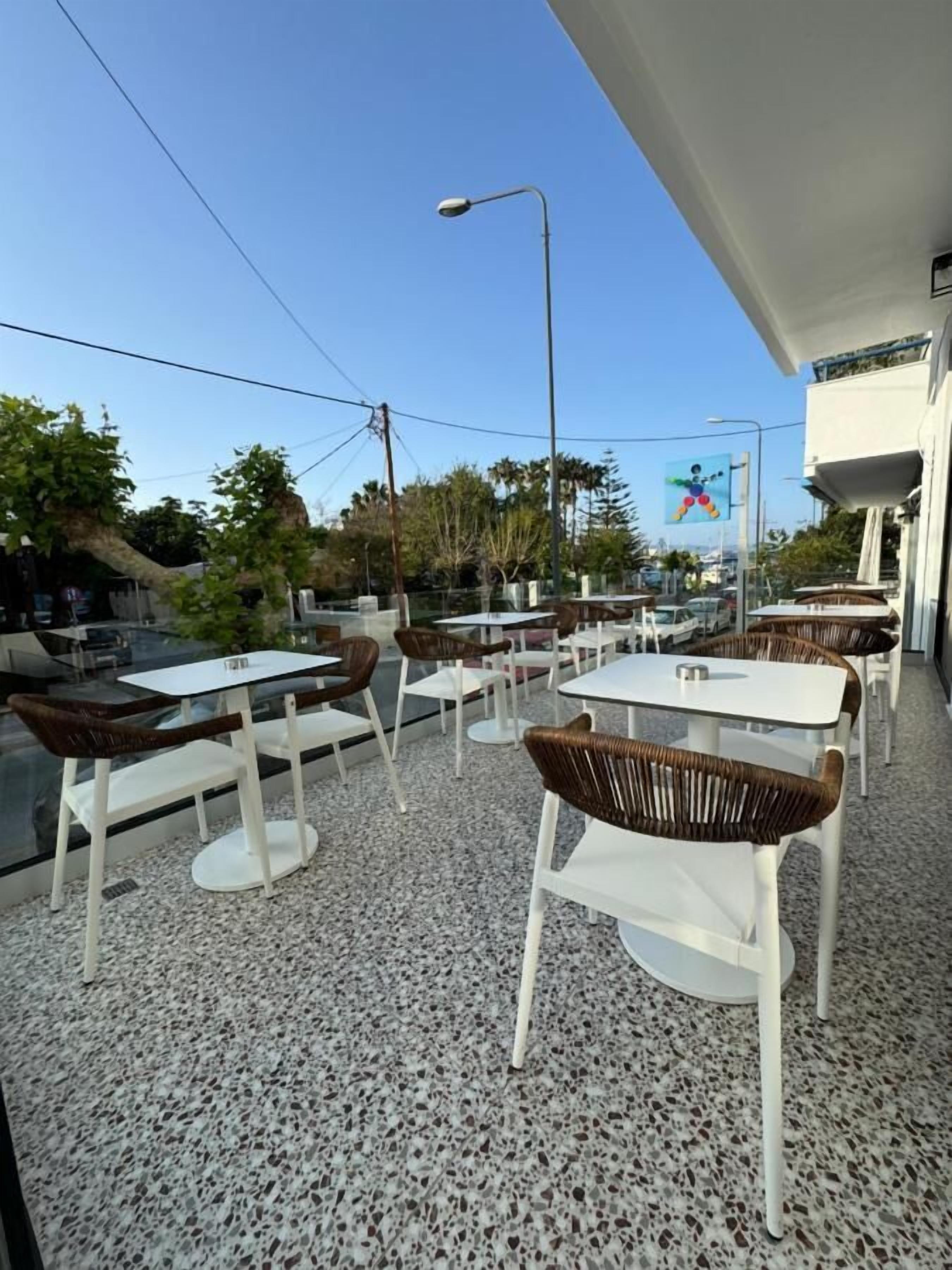 Ein Straßencafé mit Tischen und Stühlen, Blick auf die Straße und klarer Himmel.