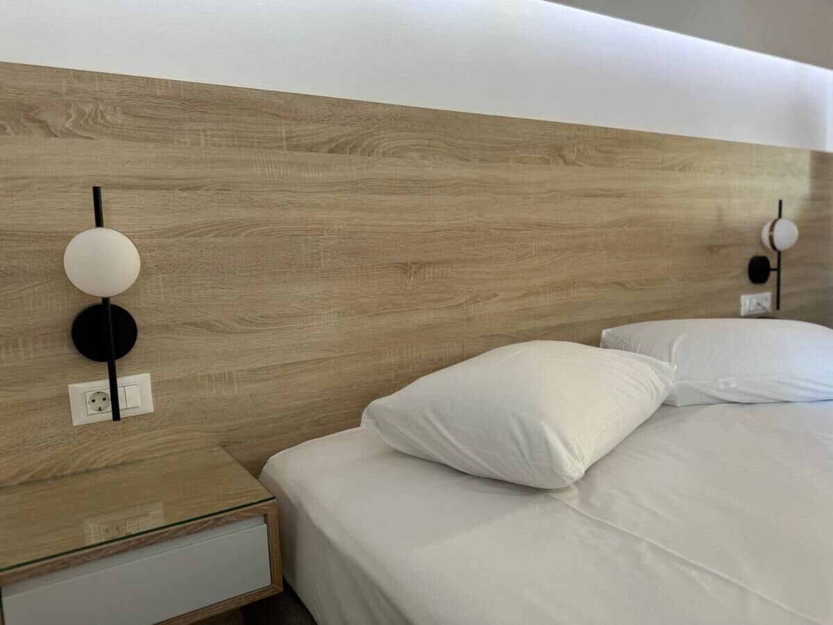 A modern hotel room with a wooden headboard, a bedside table with a lamp, and a neatly made bed with white linens.