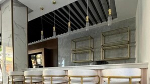 Une cuisine moderne dotée de plans de travail en marbre, de tabourets de bar dorés, de luminaires suspendus et d’un four encastré.