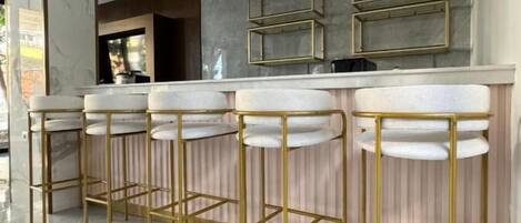 A modern kitchen with marble countertops, gold bar stools, pendant lighting, and a built-in oven.