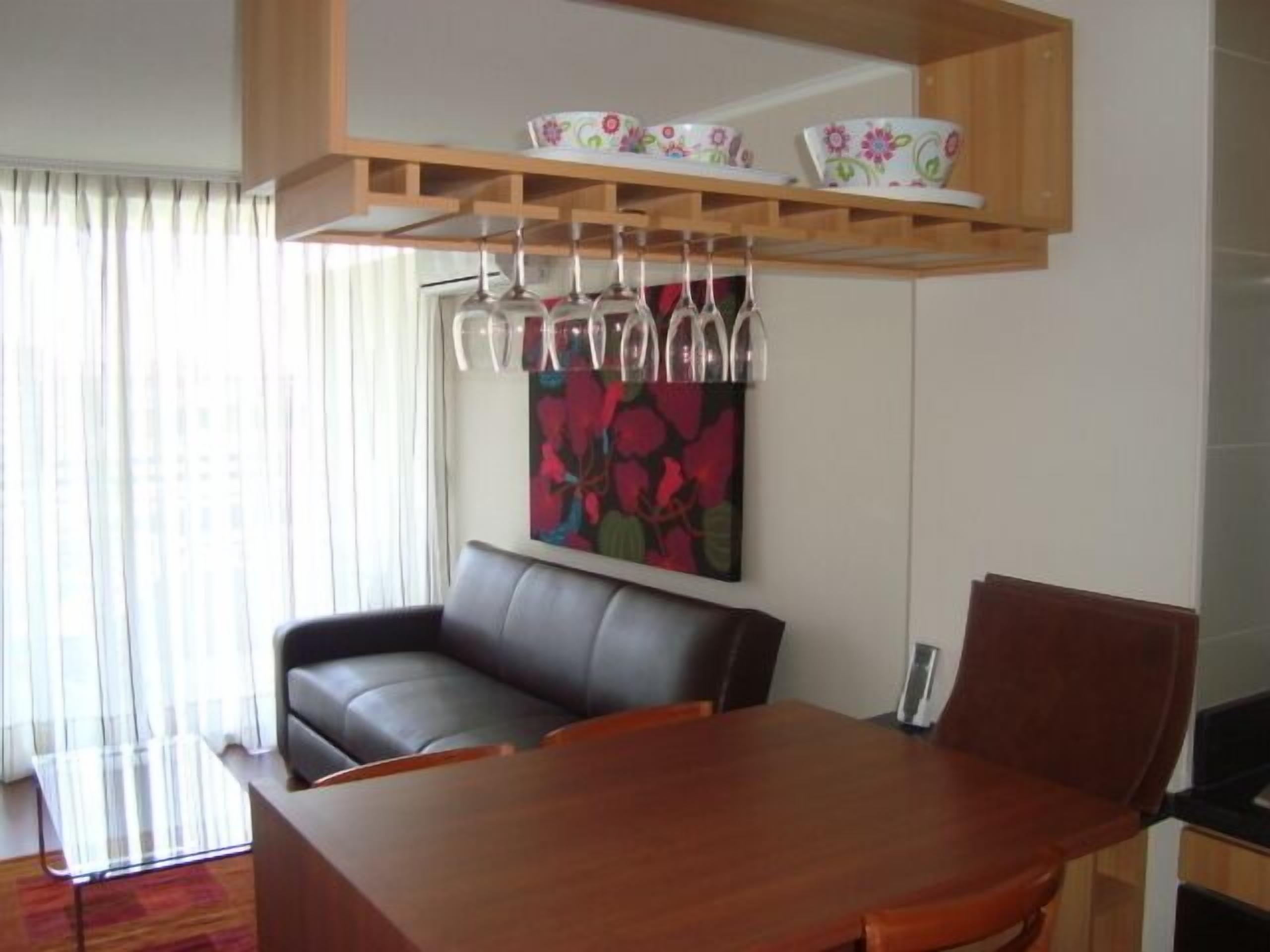 A dining area with a wooden table, a black leather sofa, and a wall-mounted shelf with cups and bowls.