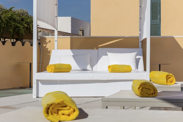 Un espace extérieur aménagé avec des sièges blancs, comprenant un canapé et deux fauteuils, chacun agrémenté d’une serviette jaune roulée.