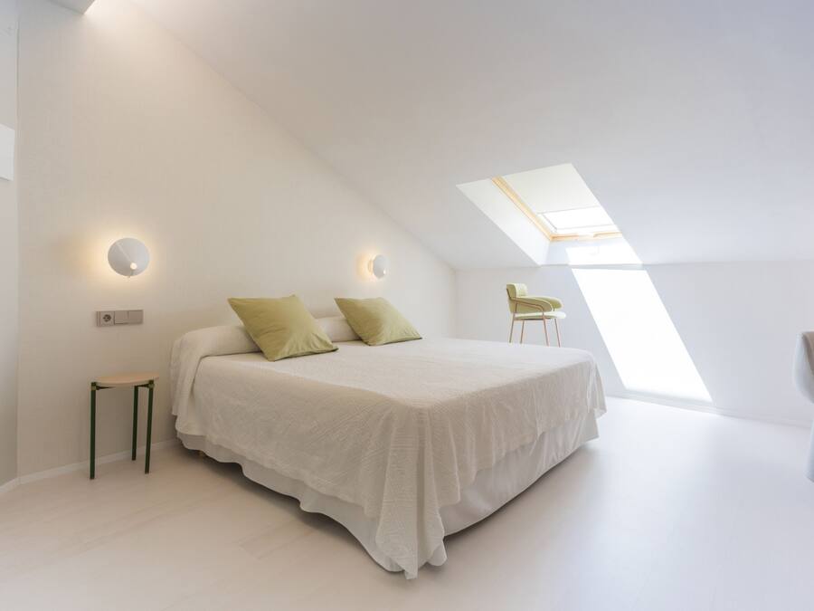 Un dormitorio moderno con una cama grande, una mesita pequeña, una silla y un tragaluz.