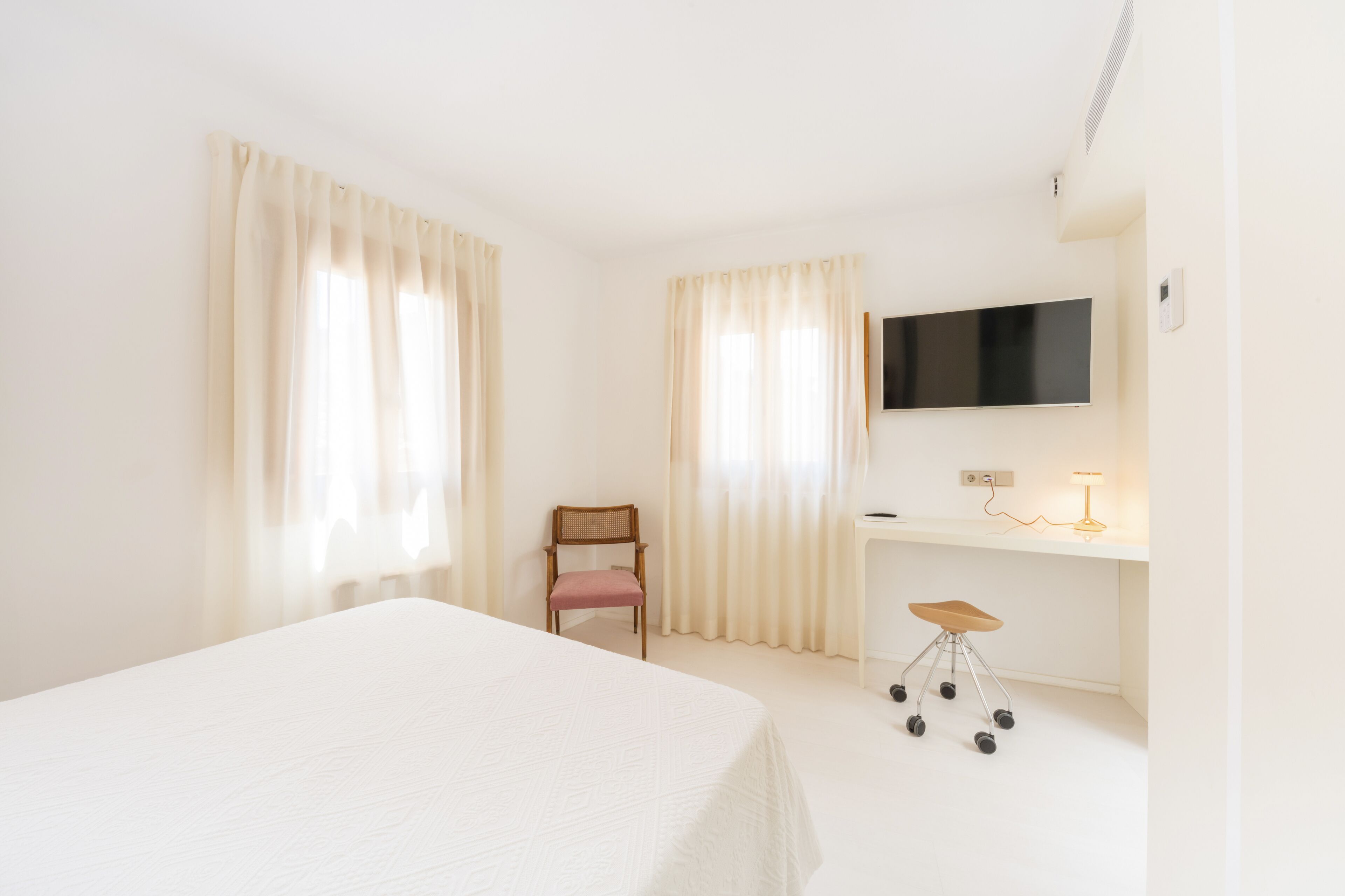 A hotel room with a bed, a desk with a chair, a television, and curtains.