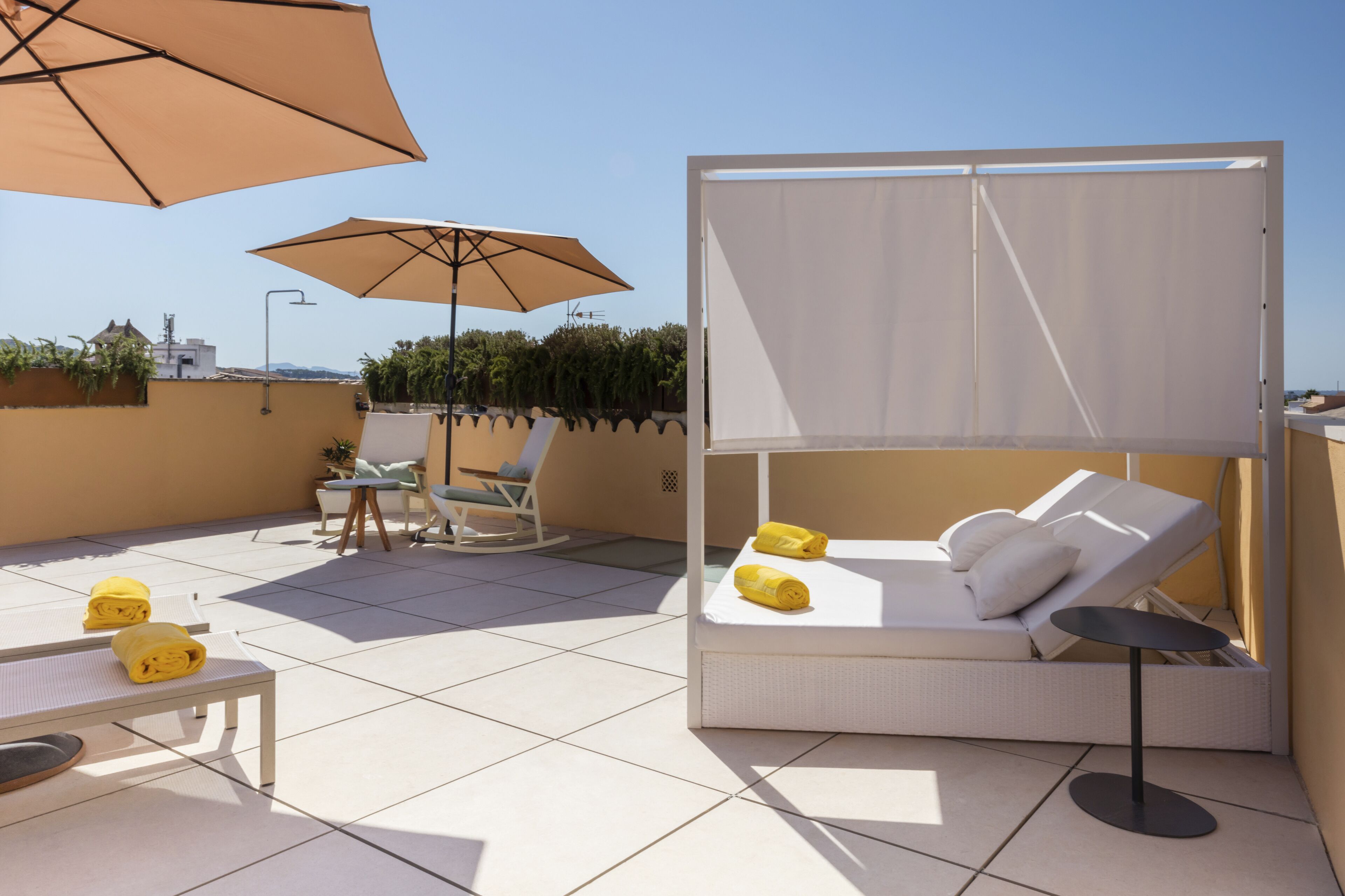 Une terrasse sur le toit équipée d’un transat, de deux fauteuils, d’une petite table et de deux grands parasols.