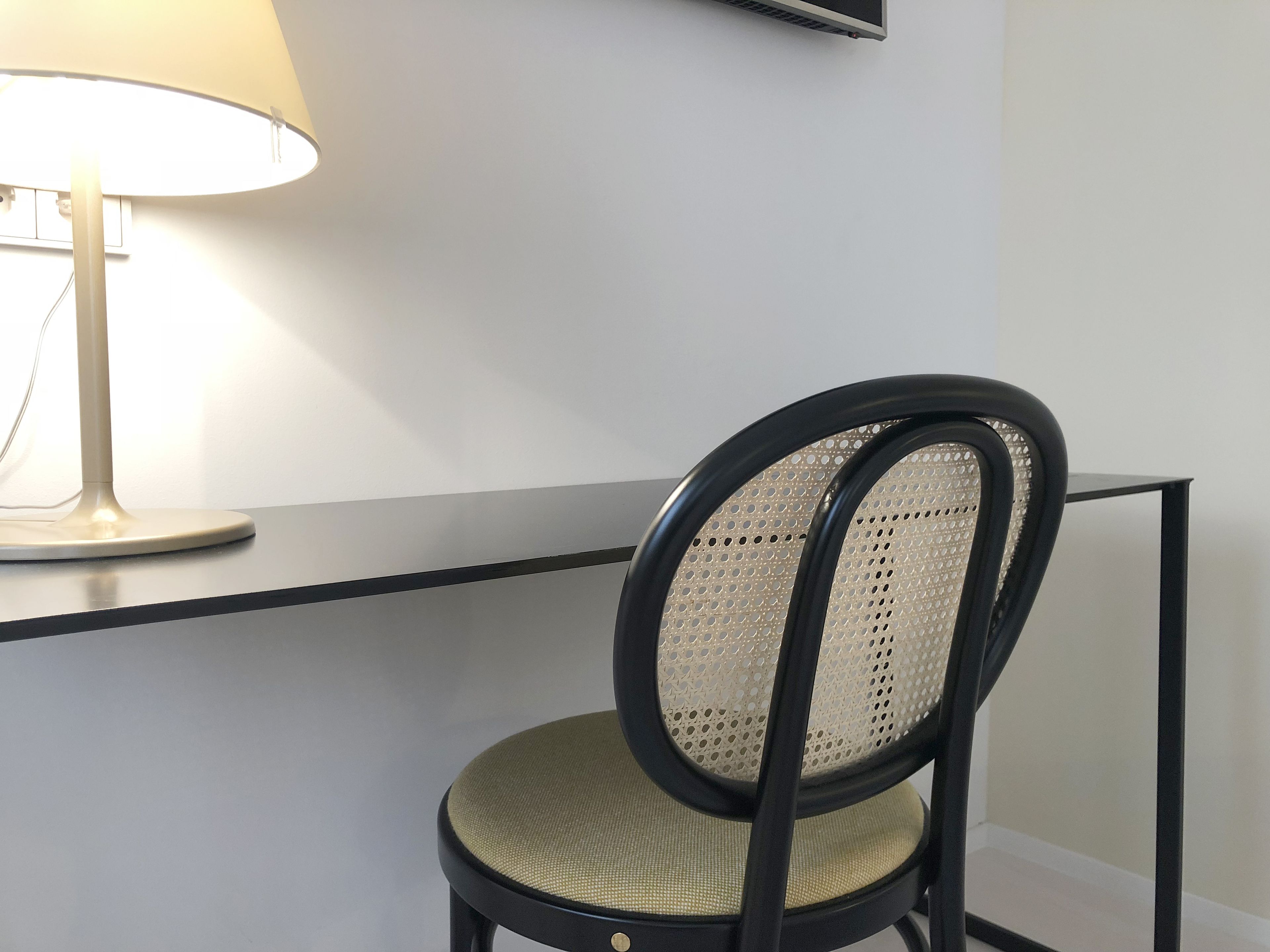 Una silla con respaldo y asiento trenzados, ubicada junto a un escritorio con una lámpara.