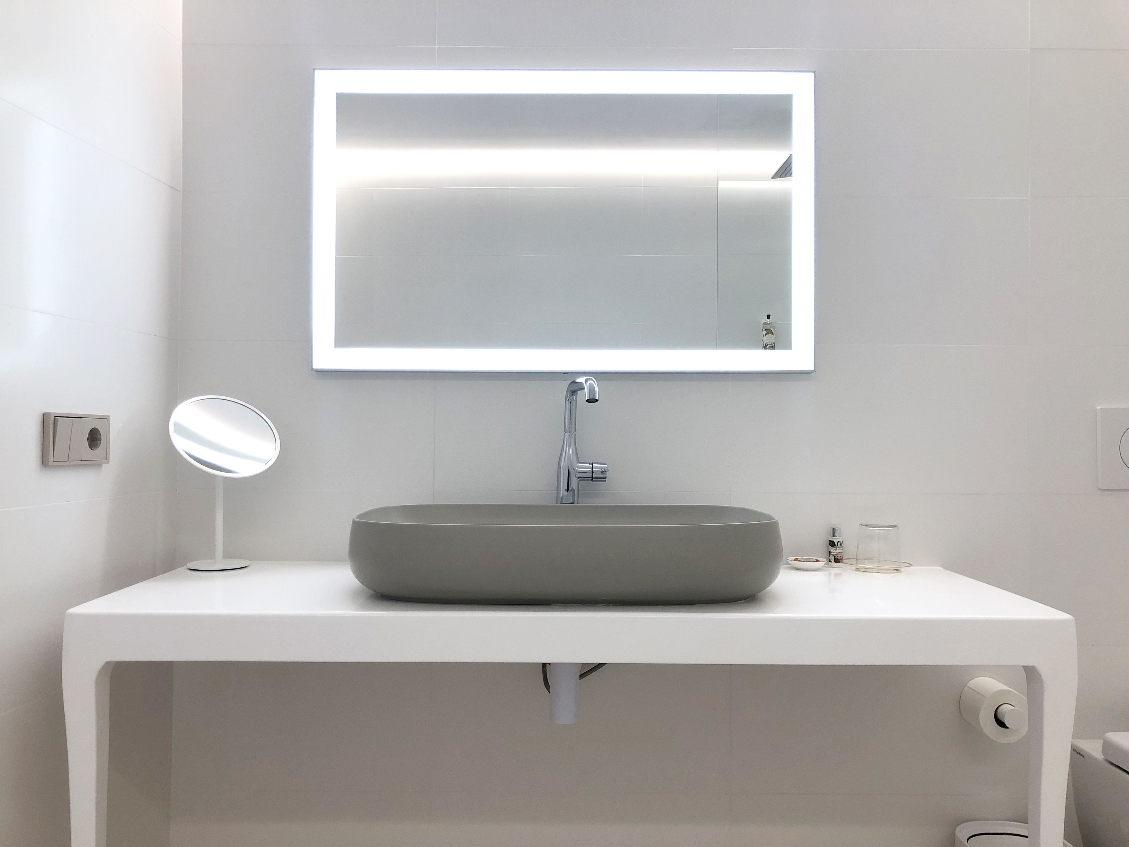 Un baño moderno con un tocador blanco, un espejo redondo y un espejo rectangular sobre el lavabo.