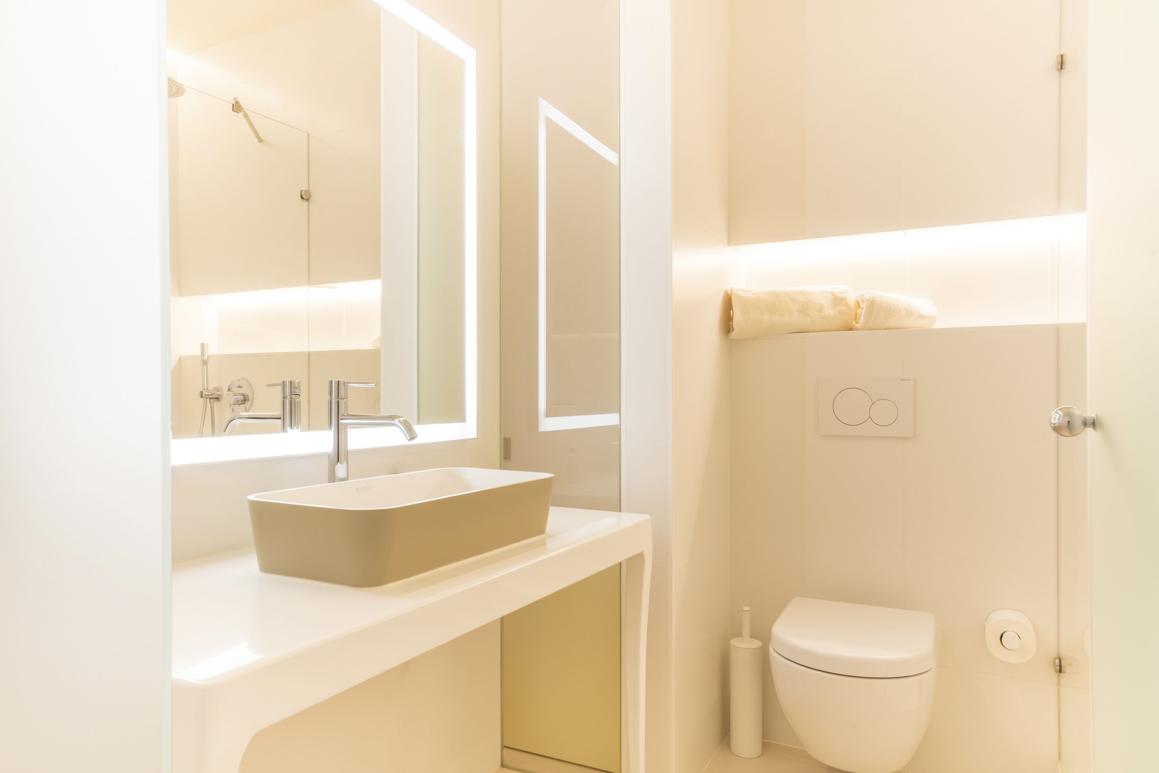 Un baño moderno con un espejo grande, un lavamanos rectangular y un inodoro.