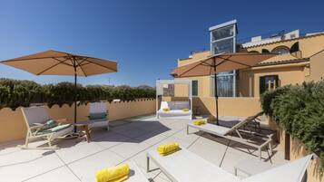 Terraza en la azotea con sillones, sombrillas y un espacio para sentarse.