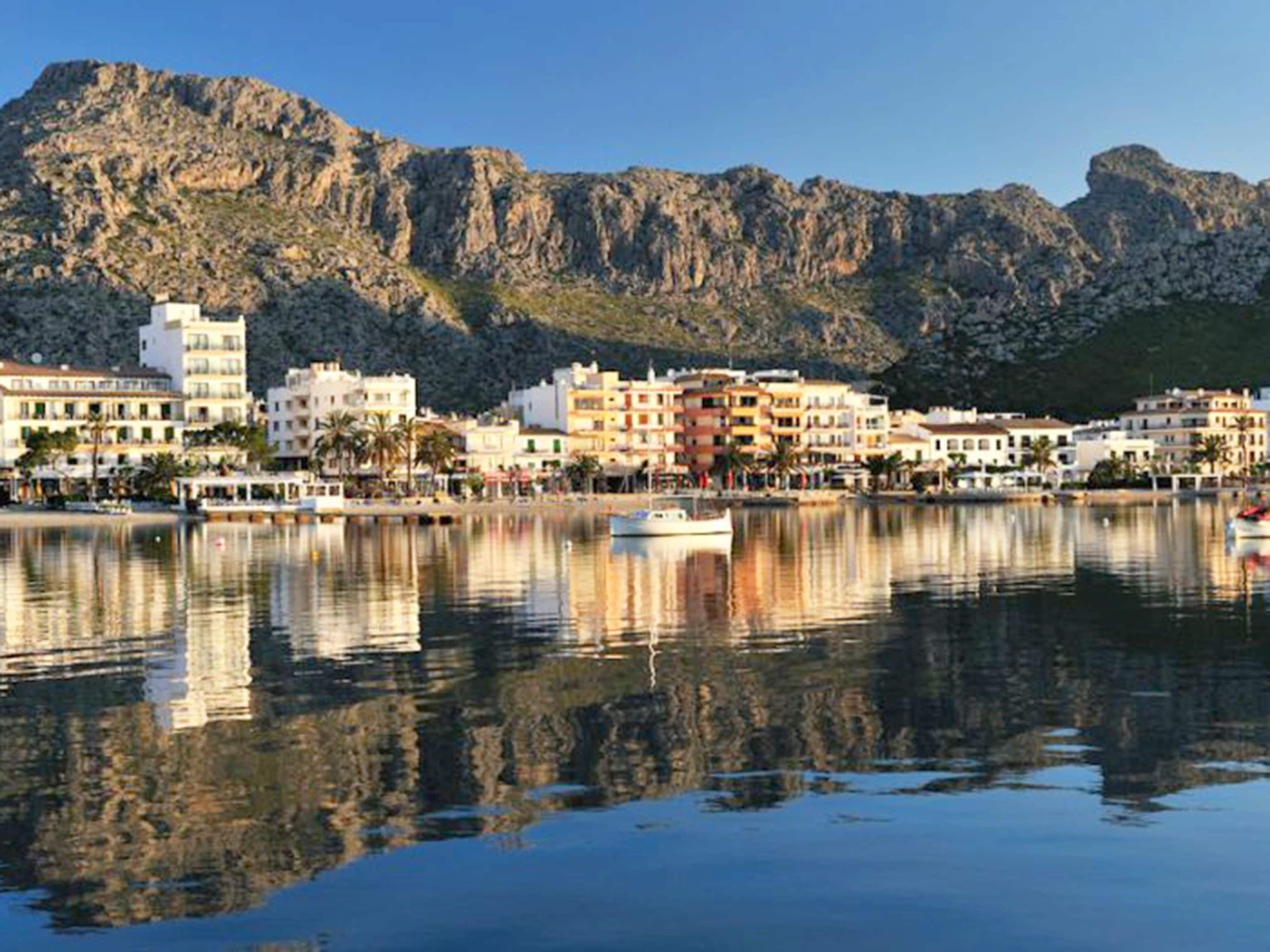 A coastal town with buildings along the waterfront, a calm sea, and mountains in the background.