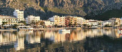 A coastal town with buildings along the waterfront, a calm sea, and mountains in the background.