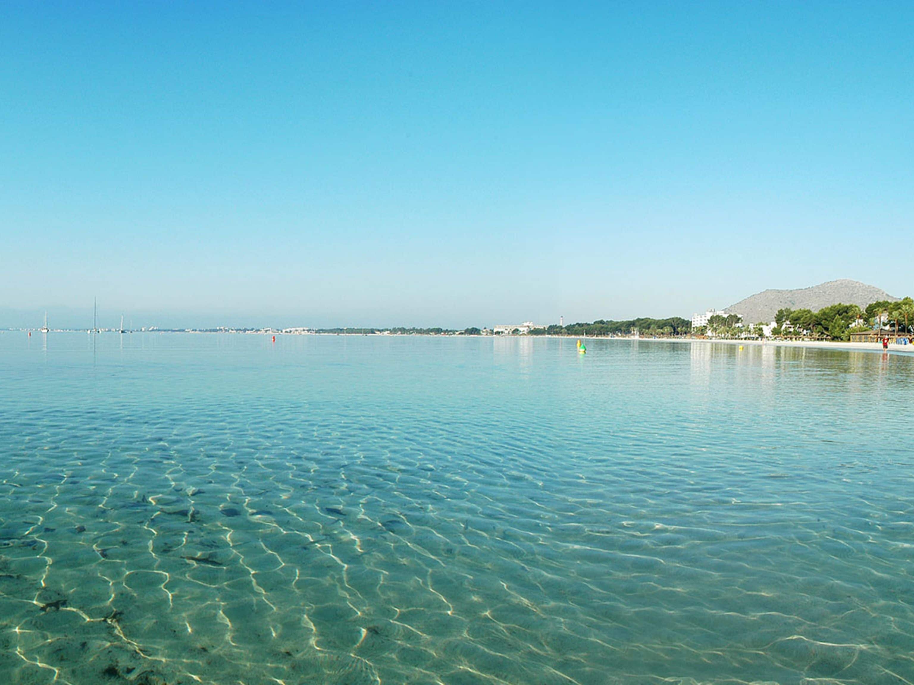A clear view of a calm sea with a distant shoreline, including buildings and a mountain.