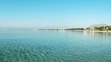 A clear view of a calm sea with a distant shoreline, including buildings and a mountain.