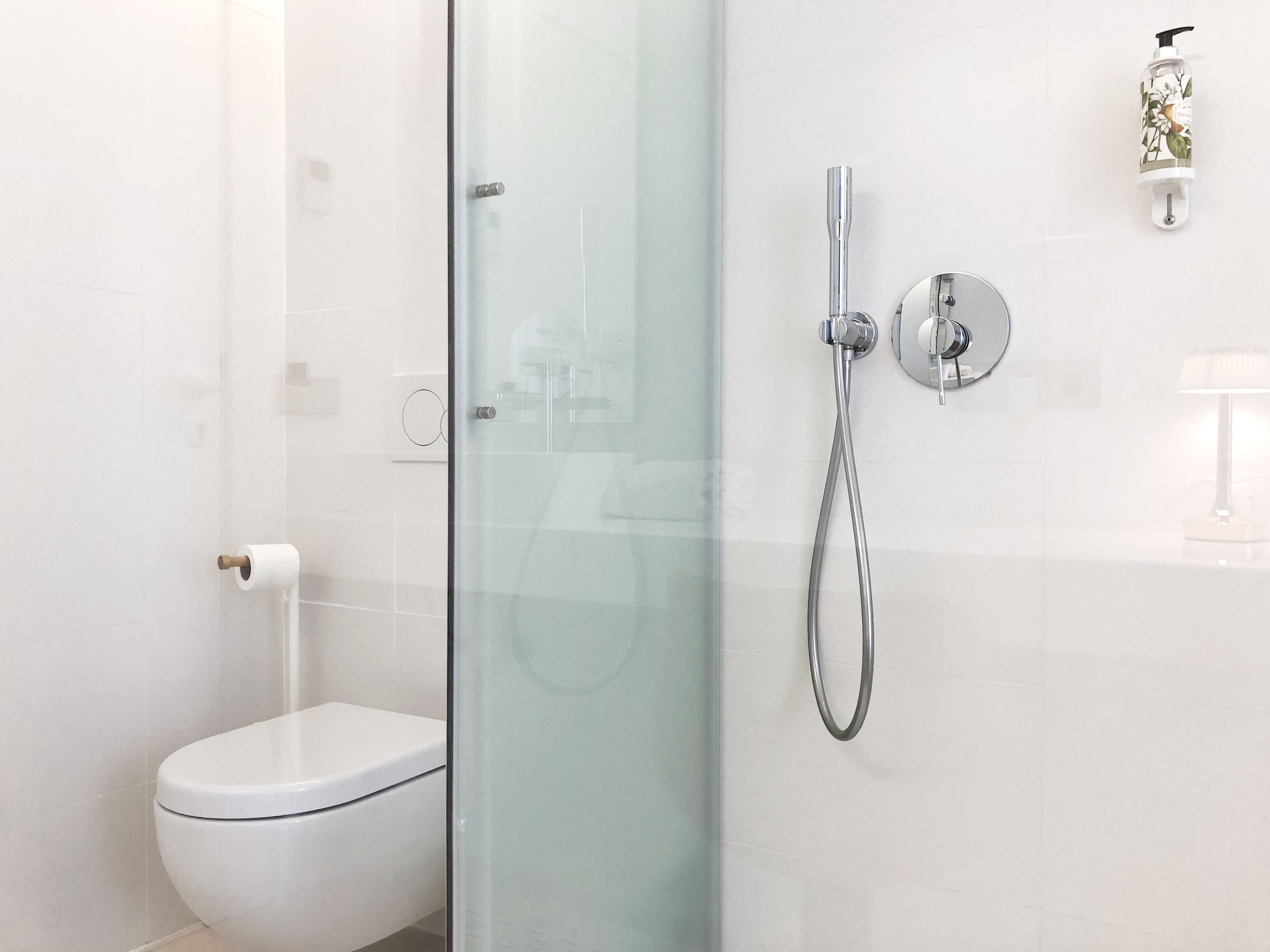 A modern bathroom with a glass shower enclosure, a toilet, and a wall-mounted hand dryer.