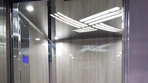 An elevator with a metallic interior, control panel with buttons, and a patterned wall. - Hotel Sonia (Kos)