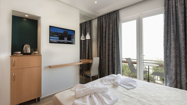 A hotel room with a bed, a desk, a chair, a TV, and a balcony with curtains. - Hotel Sonia (Kos)