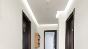 A modern hallway with a wooden bookshelf, dark doors, and a tiled floor. - Hotel Sonia (Kos)