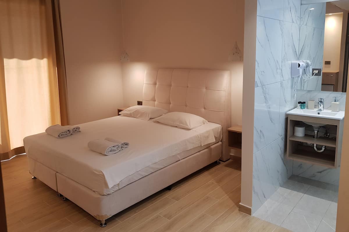 A hotel room with a large bed, a bedside table, a built-in bathroom with a sink, and a mirror.