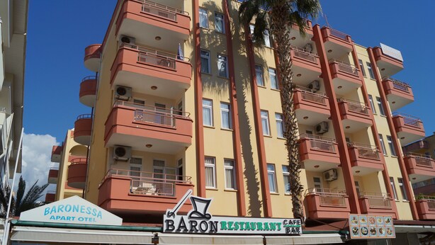 Un immeuble à plusieurs étages doté de balcons, une enseigne indiquant « Baron Restaurant & Bar » et une autre indiquant « Baronesssa Apart Hotel ».