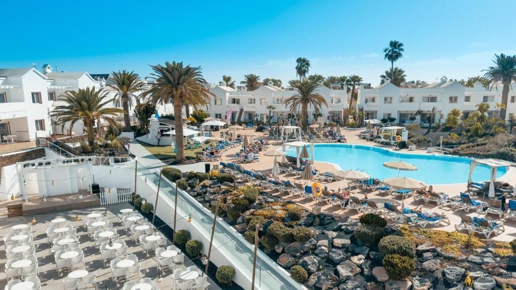 A resort with a large pool, palm trees, and a terrace with tables and chairs.