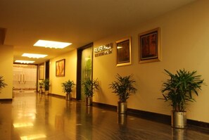 Um hall de hotel com piso de madeira envernizada, plantas em vasos, obras de arte emolduradas e um letreiro para 'SILVER PALM WINE & RESTAURANT'.