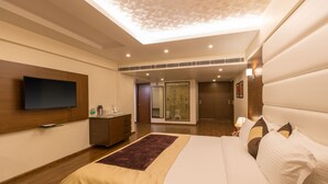 A modern hotel room with a large bed, a flat-screen TV, a wooden dresser, and a bathroom visible through a glass door. - Hotel Softel Plaza (Dehradun)