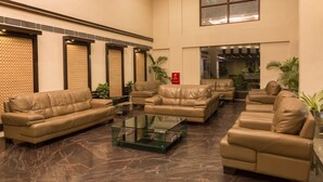 A spacious lobby with leather sofas and a glass coffee table, large windows, and potted plants. - Hotel Softel Plaza (Dehradun)