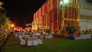 An outdoor event space with tables and chairs arranged for guests, surrounded by a building with string lights and greenery. - Hotel Softel Plaza (Dehradun)