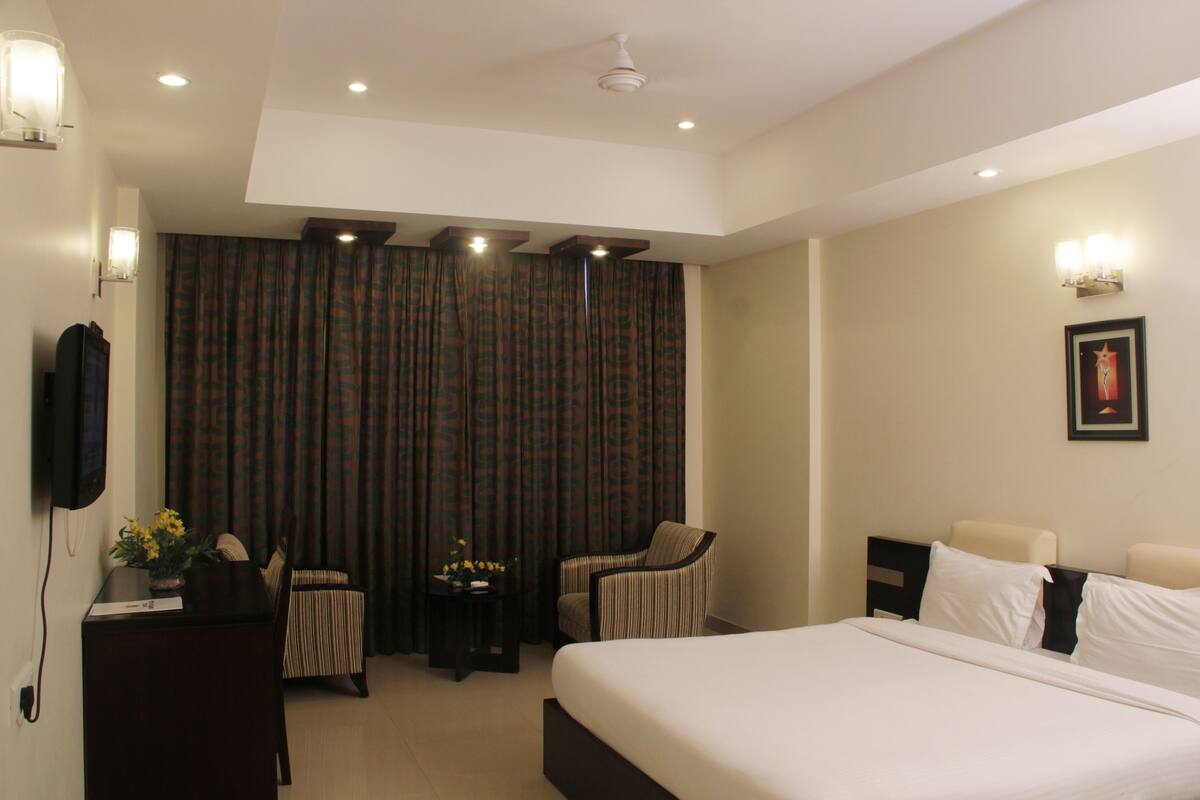 A hotel room with a large bed, a desk with a chair, a small table with flowers, and curtains.
