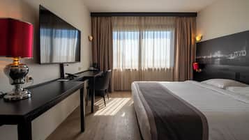 Een hotelkamer met een bed, bureau, stoel, televisie en gordijnen.